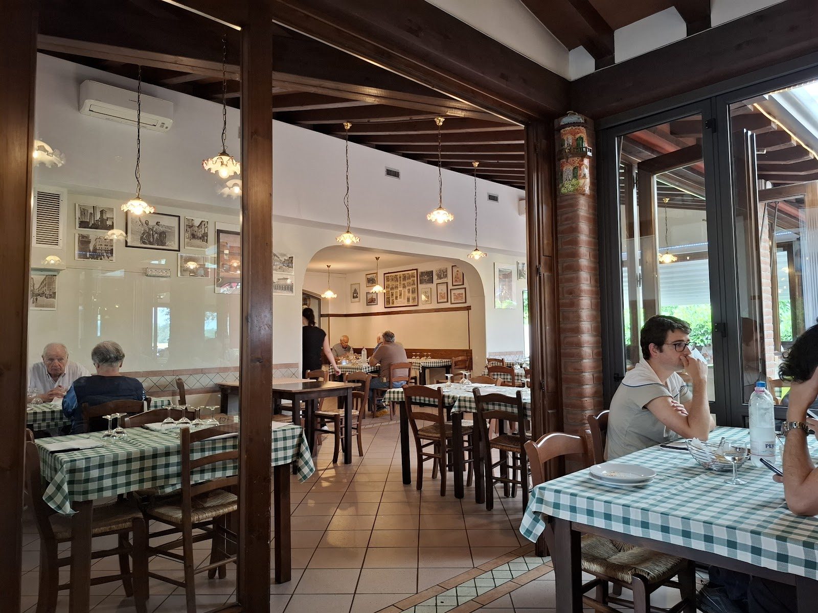 La sala della Trattoria Sandoni: legno, mattoni a vista, tovaglie a quadri e foto in bianco e nero alle pareti