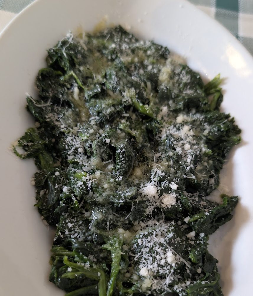 Spinaci saltati con olio e parmigiano, su tovaglia a quadri verde